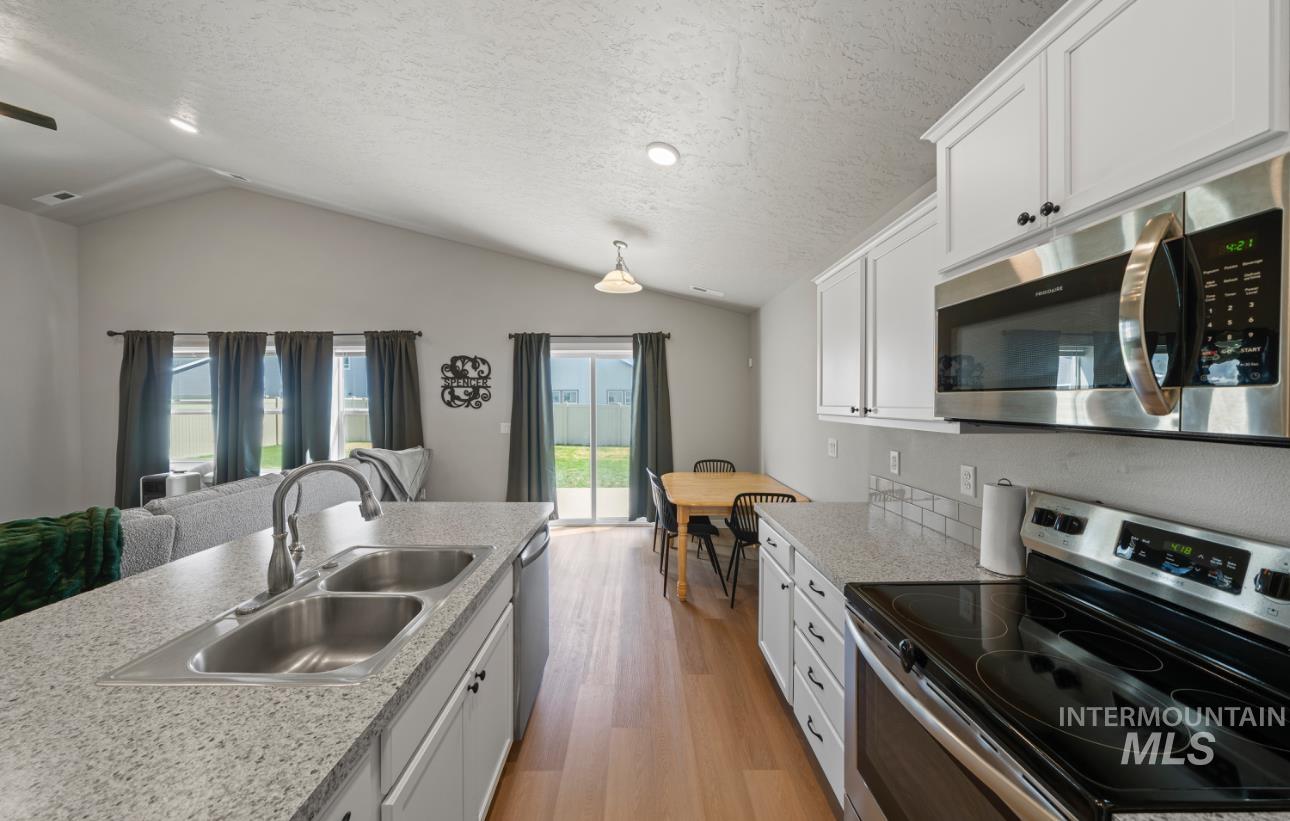 12443 Varga Street Caldwell, ID 83607 - Photo 6 of 27 Kitchen with stainless steel appliances, light wood-type flooring, white cabinetry, lofted ceiling, and a textured ceiling