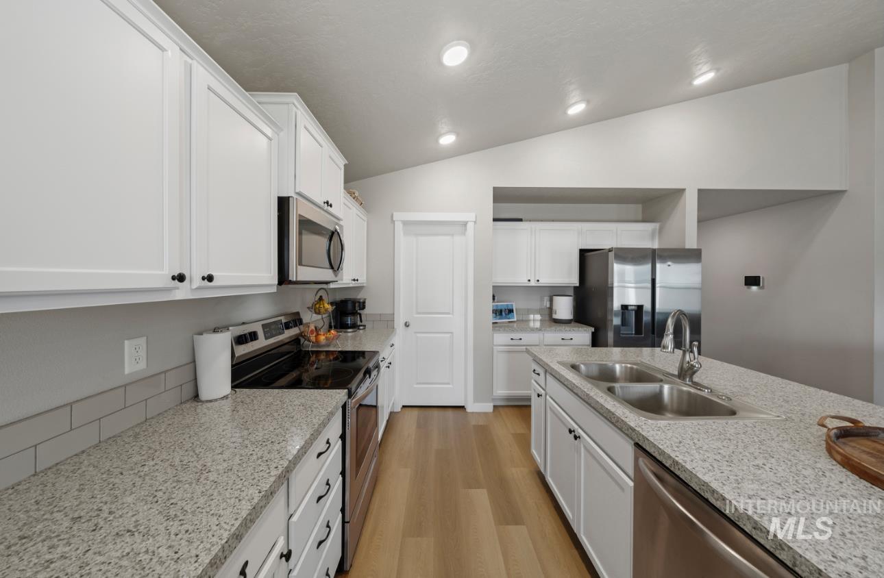 12443 Varga Street Caldwell, ID 83607 - Photo 10 of 27 Kitchen featuring stainless steel appliances, lofted ceiling, light wood-style flooring, white cabinetry, and light stone counters