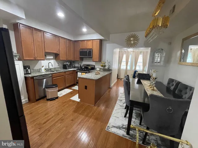 a kitchen with kitchen island a stove a refrigerator a sink a dining table and chairs with wooden floor