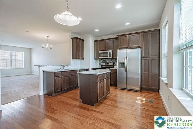 a kitchen with kitchen island granite countertop wooden floors stainless steel appliances a sink and a window