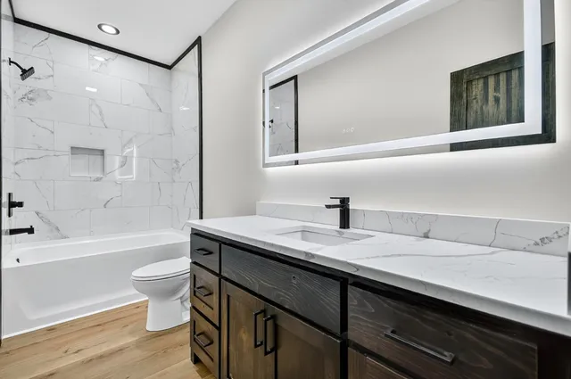 a bathroom with a granite countertop sink a toilet a mirror and bathtub