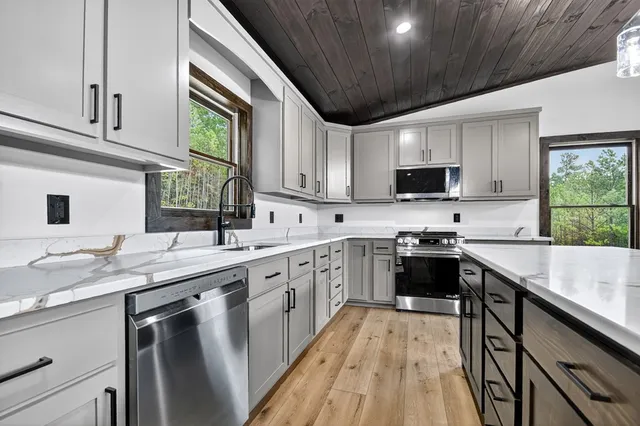 a kitchen with stainless steel appliances granite countertop a sink a stove top oven a refrigerator cabinets and a dining table with wooden floor