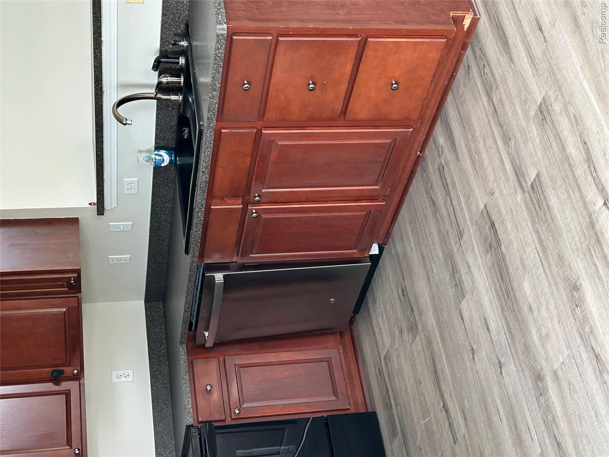 4256 Hampton Ridge Boulevard Howell, MI 48843 - Photo 9 of 25 Wood-finish flooring with rich wood cabinetry, stainless steel dishwasher, dark countertop, and black sink with a gooseneck faucet