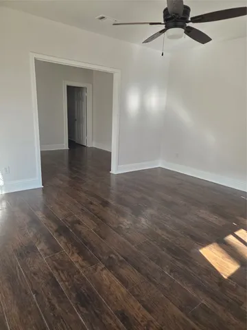 a view of an empty room with wooden floor and a ceiling fan