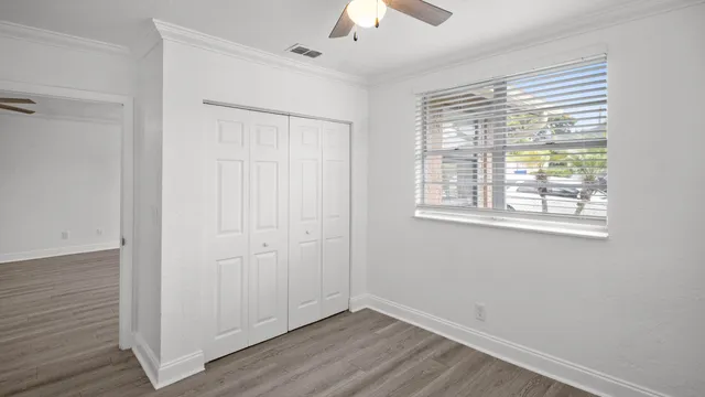 a view of an empty room with wooden floor closet and a window