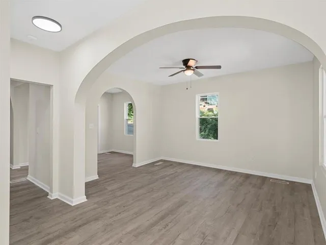 an empty room with wooden floor chandelier fan and windows