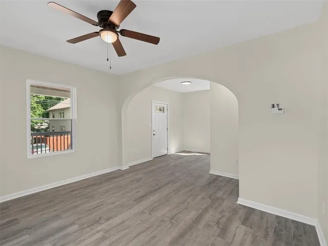 an empty room with wooden floor ceiling fan and windows