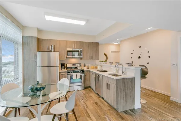a kitchen with stainless steel appliances granite countertop a stove a refrigerator a sink a dining table and chairs with wooden floor
