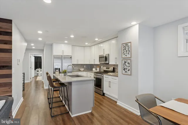 a kitchen with stainless steel appliances kitchen island granite countertop a stove a sink a refrigerator and white cabinets with wooden floor