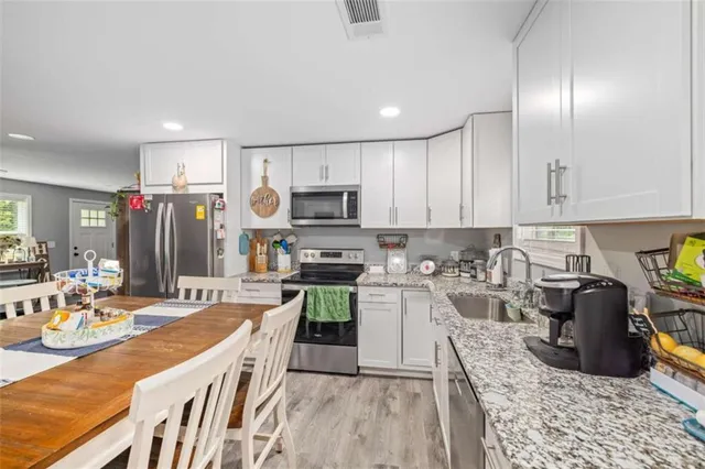 a kitchen with stainless steel appliances granite countertop a refrigerator a stove top oven a sink dishwasher and white cabinets with wooden floor