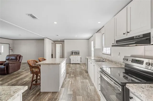 a kitchen with stainless steel appliances granite countertop a stove top oven a sink dishwasher and white cabinets with wooden floor