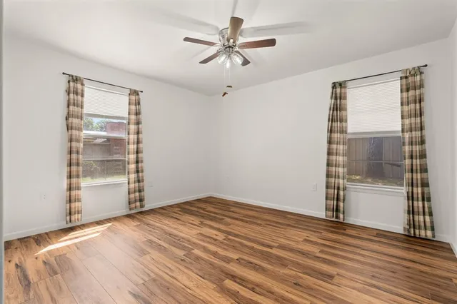 an empty room with wooden floor fan and windows