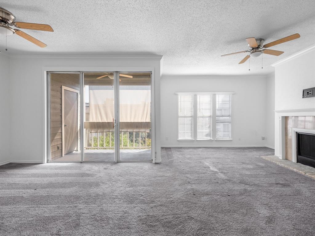 5310 Keller Springs Road, Unit 332 Dallas, TX 75248 - Photo 19 of 39 Unfurnished living room featuring ceiling fan, carpet floors, a textured ceiling, a fireplace with raised hearth, and crown molding