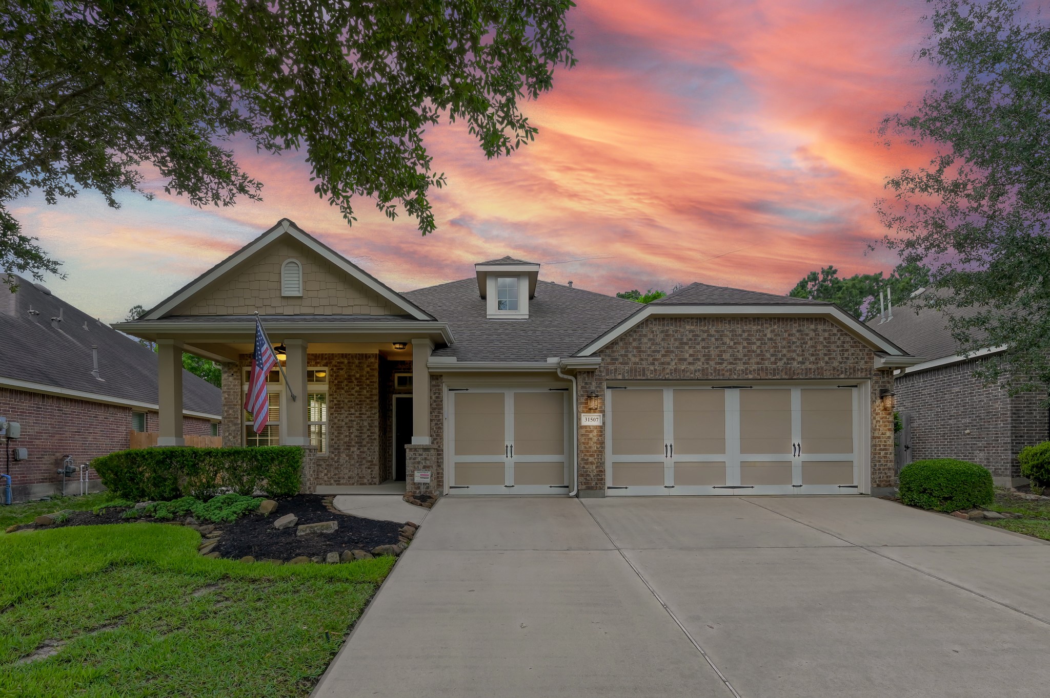 Charming single-story brick home with a spacious three-car garage, welcoming front porch, and manicured landscaping. Set against a beautiful sunset sky, this property offers a cozy and inviting curb appeal.