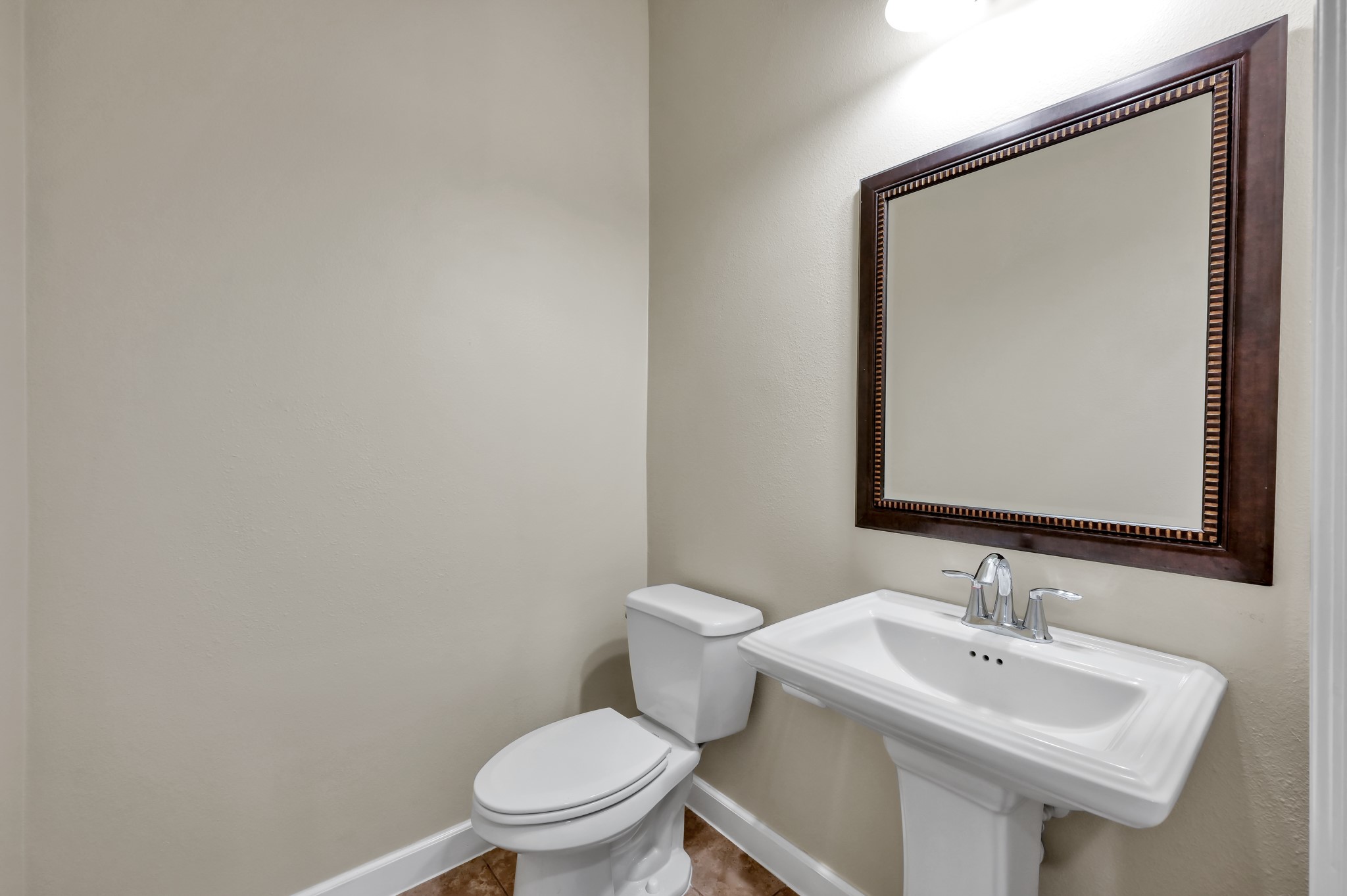 31507 Boulder Cliff Lane Spring, TX 77386 - Photo 11 of 45 This is a compact, well-lit half bathroom featuring a pedestal sink, a toilet, and a large framed mirror. The neutral color scheme and simple design create a clean and functional space.
