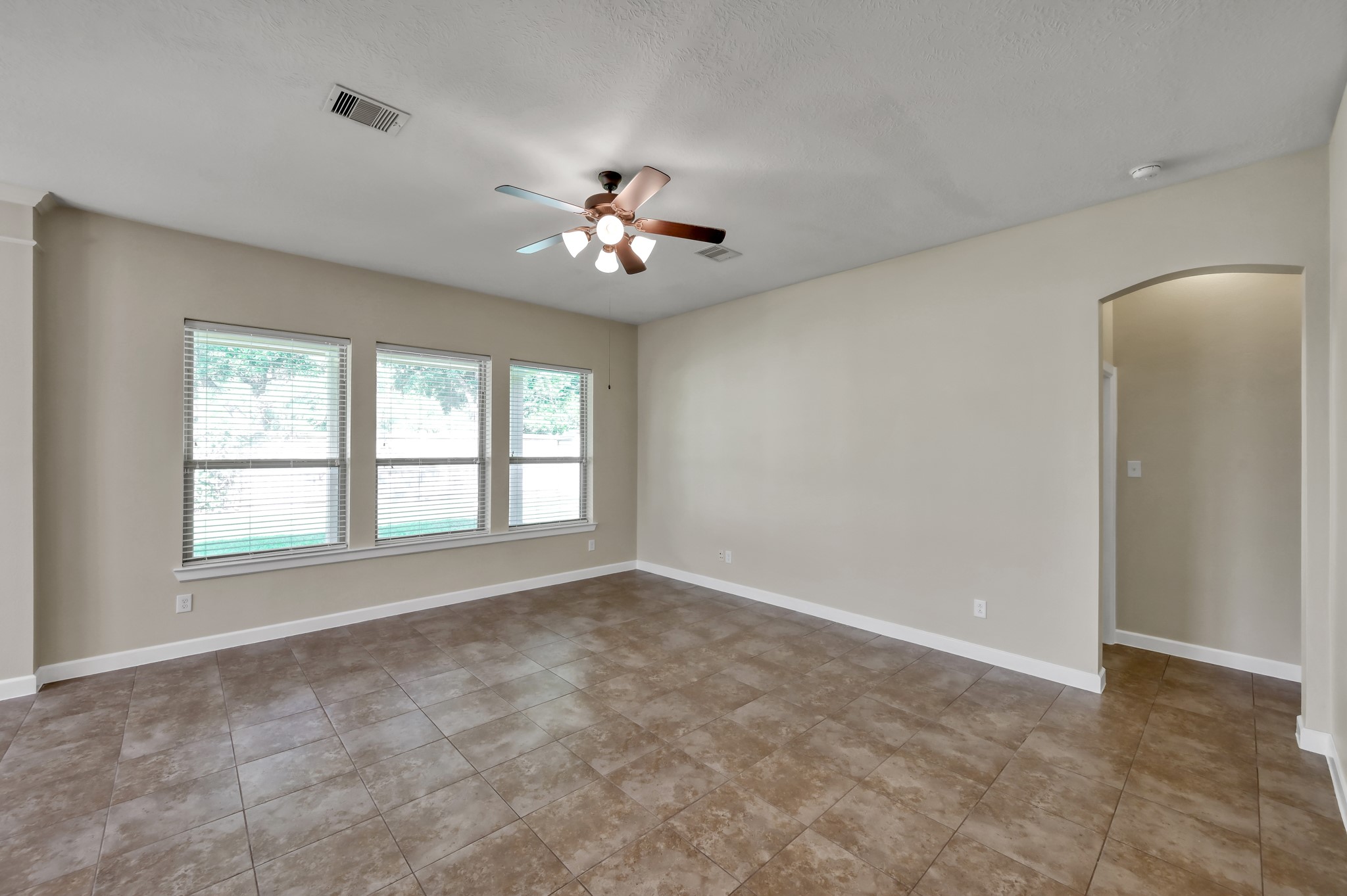 31507 Boulder Cliff Lane Spring, TX 77386 - Photo 12 of 45 Bright and spacious living area with large windows, neutral walls, and tiled flooring. Features a ceiling fan and an arched doorway, providing a modern and inviting feel.