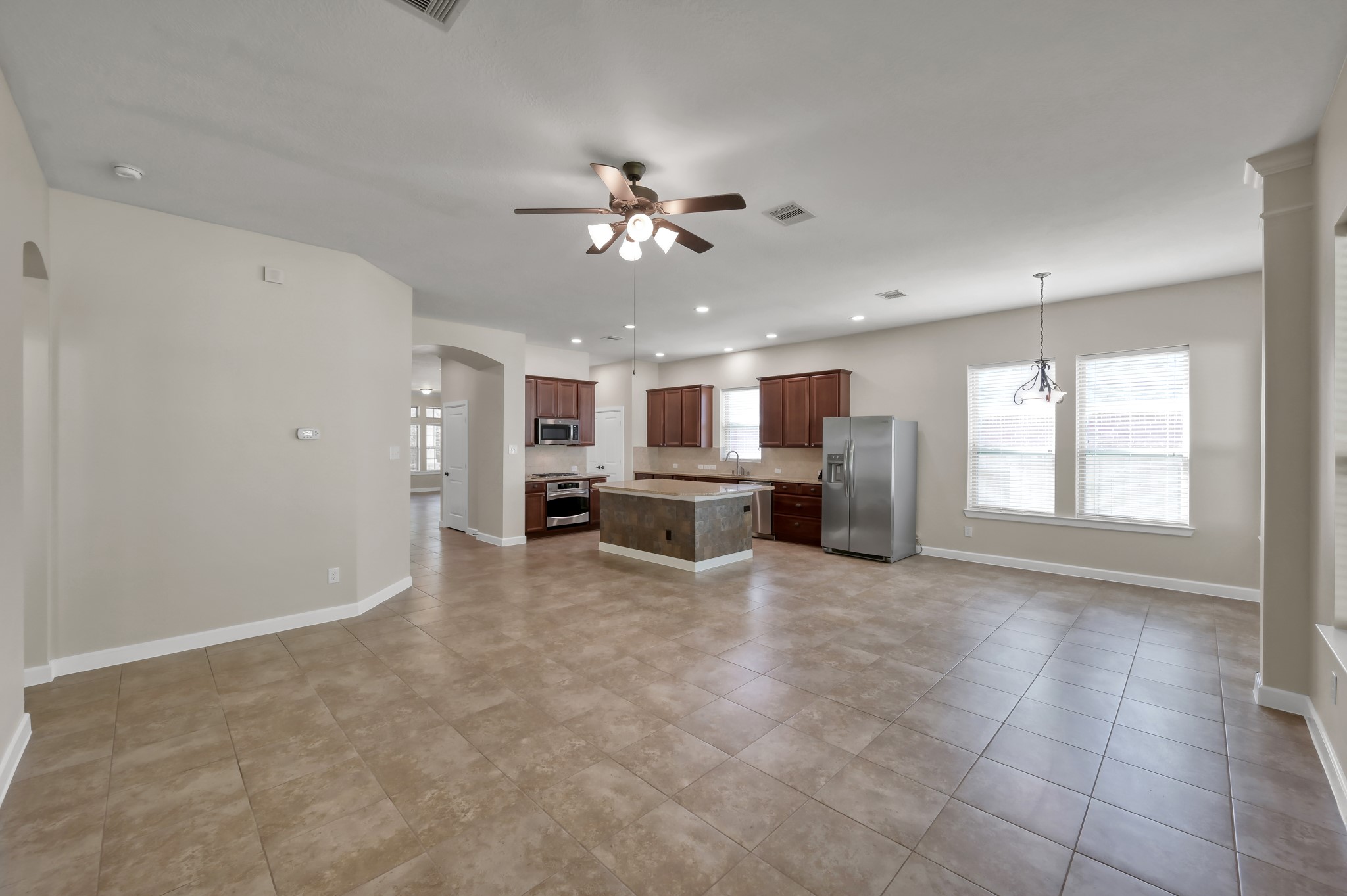 31507 Boulder Cliff Lane Spring, TX 77386 - Photo 14 of 45 This spacious open-concept living area features a modern kitchen with stainless steel appliances, an island, and ample cabinetry. The room is brightened by natural light from large windows, and the neutral tile flooring complements the contemporary design. A ceiling fan adds comfort, making it ideal for entertaining.