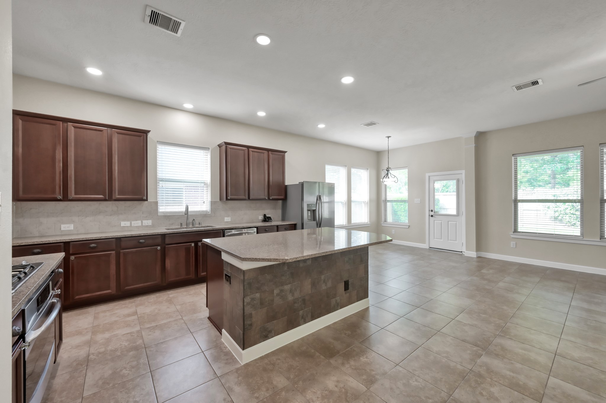 31507 Boulder Cliff Lane Spring, TX 77386 - Photo 16 of 45 Spacious open-concept kitchen and dining area with modern tile flooring, ample natural light, and elegant dark wood cabinetry. Features a central island, stainless steel appliances, and large windows overlooking the backyard.
