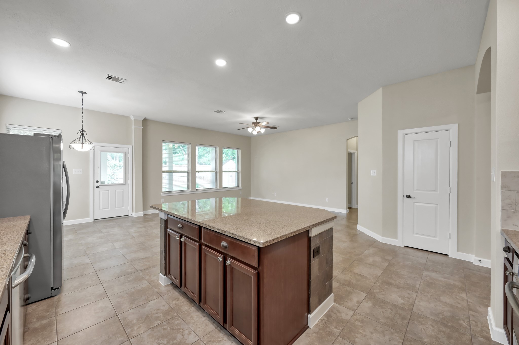 31507 Boulder Cliff Lane Spring, TX 77386 - Photo 17 of 45 This photo showcases a spacious open-concept kitchen and living area with tiled floors, a large central island, ample natural light from multiple windows, and neutral-colored walls for a modern, airy feel.