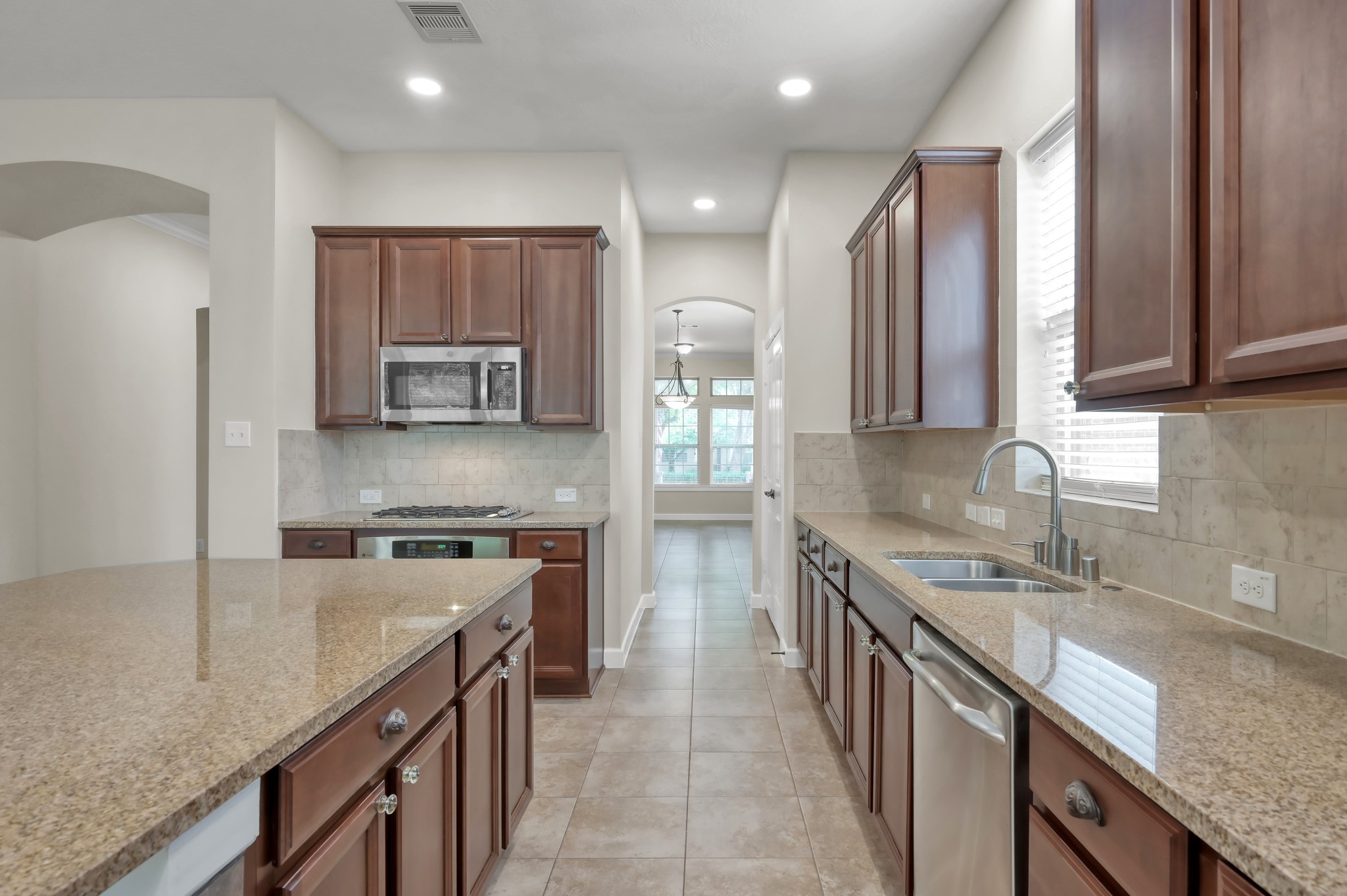 31507 Boulder Cliff Lane Spring, TX 77386 - Photo 18 of 45 This photo showcases a modern kitchen with granite countertops, stainless steel appliances, and rich wooden cabinetry. It features a spacious layout with ample natural light and a view into a dining area through an arched passageway.