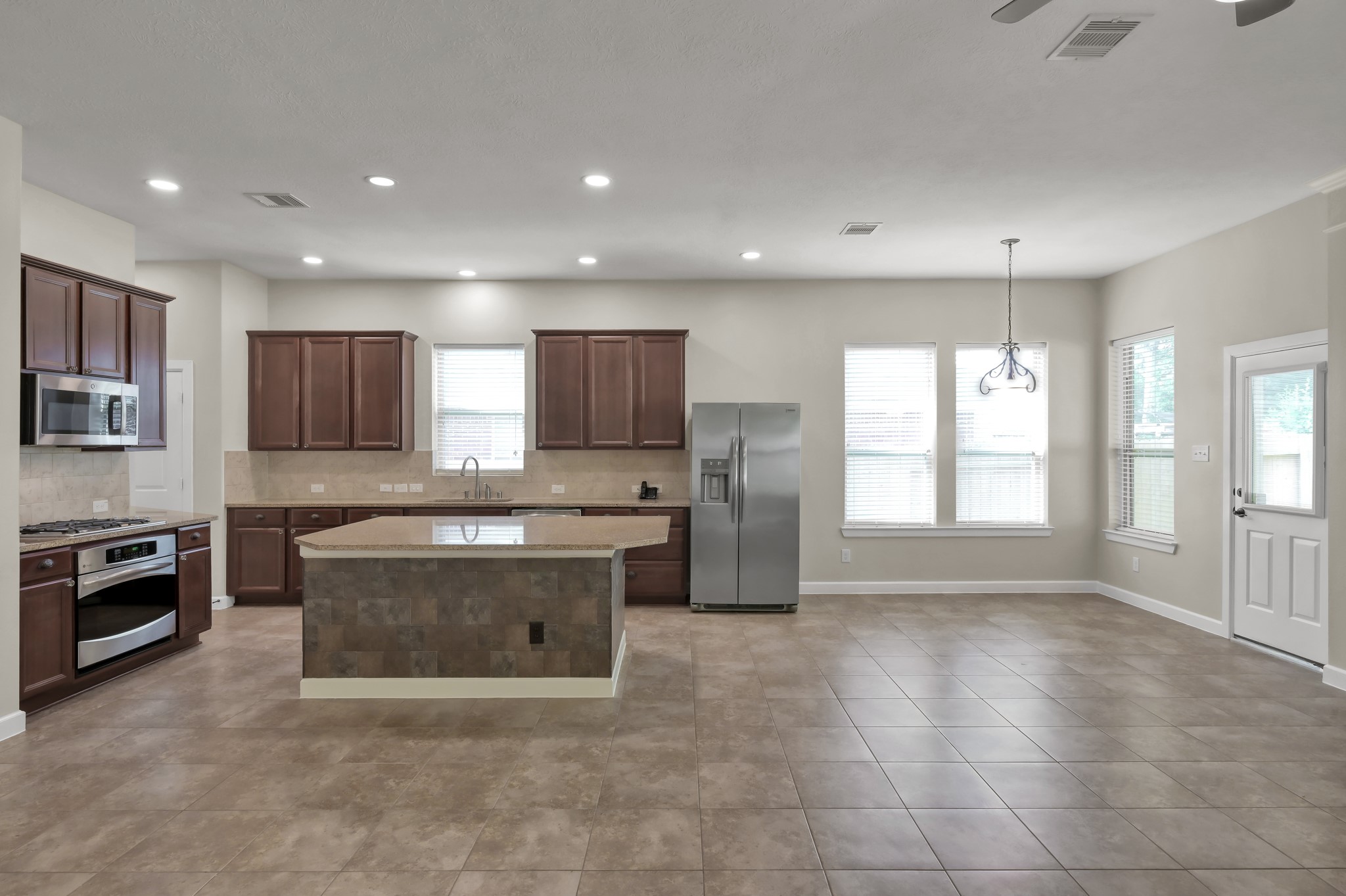 31507 Boulder Cliff Lane Spring, TX 77386 - Photo 22 of 45 This open-concept kitchen features dark wood cabinets, a central island, stainless steel appliances, and large windows for natural light. The spacious area has tile flooring and an adjacent dining space, perfect for entertaining.