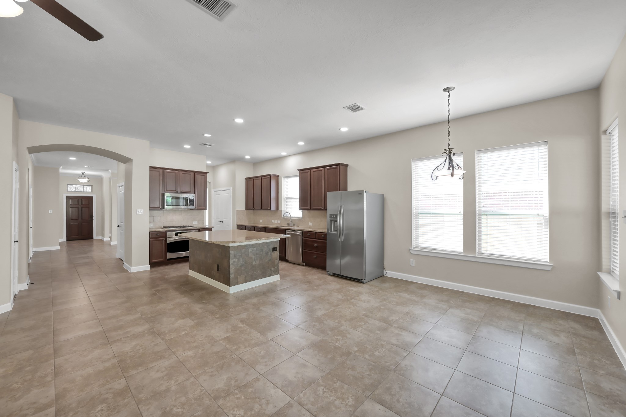 31507 Boulder Cliff Lane Spring, TX 77386 - Photo 23 of 45 This spacious, open-concept kitchen and living area features modern tile flooring, recessed lighting, and ample natural light. The kitchen includes dark wood cabinetry, a center island, stainless steel appliances, and a dining area with large windows.