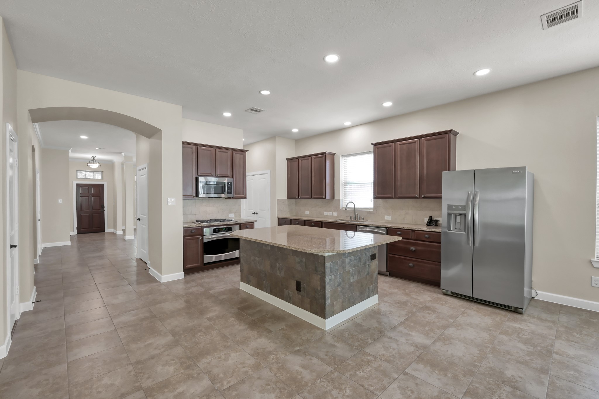 31507 Boulder Cliff Lane Spring, TX 77386 - Photo 24 of 45 A spacious kitchen with modern stainless steel appliances, dark wood cabinets, and a large central island. The room features recessed lighting, neutral tile flooring, and an open layout that flows into a bright hallway.