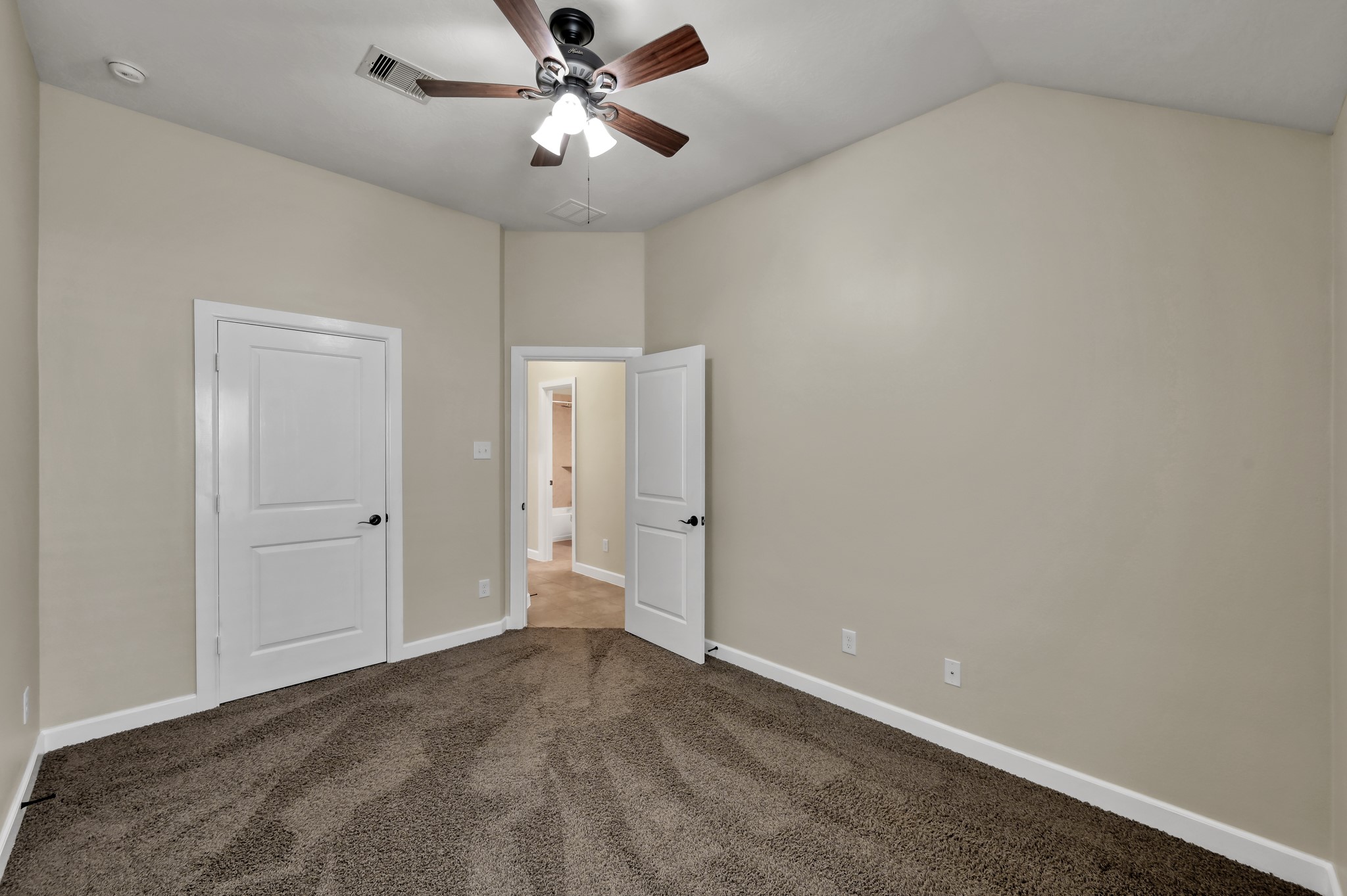 31507 Boulder Cliff Lane Spring, TX 77386 - Photo 32 of 45 This photo shows a small, neutral-toned room with carpeted flooring, a ceiling fan, and two white doors. One door is closed, and the other leads to an adjacent space, offering a cozy, versatile area for various uses.