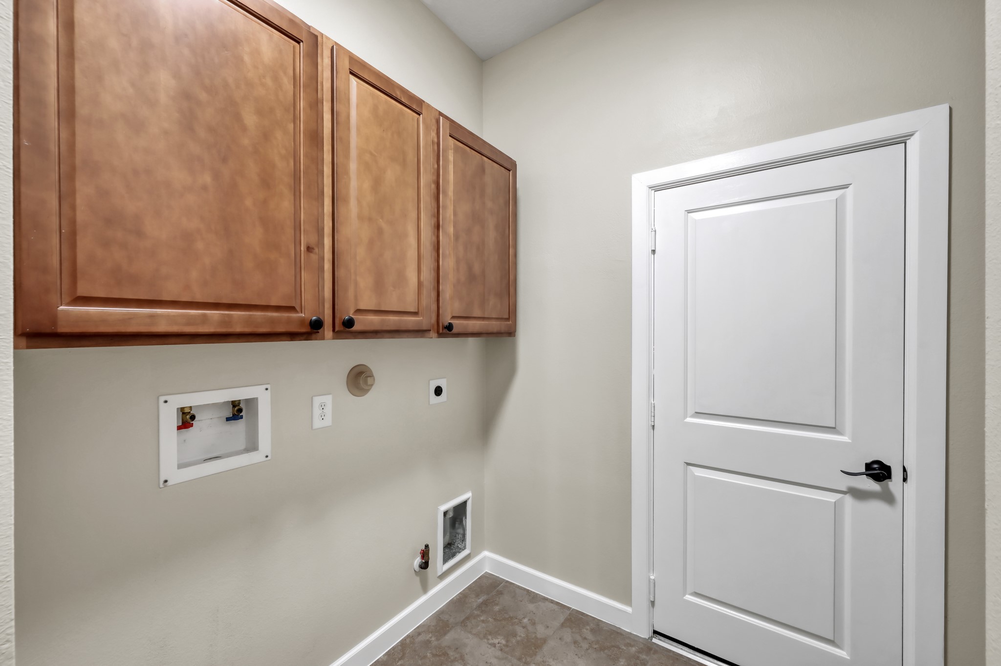 31507 Boulder Cliff Lane Spring, TX 77386 - Photo 33 of 45 This is a utility room featuring upper wooden cabinets for storage, plumbing hookups for a washer and dryer, and a white door with a sleek handle. The space has neutral walls and tile flooring.