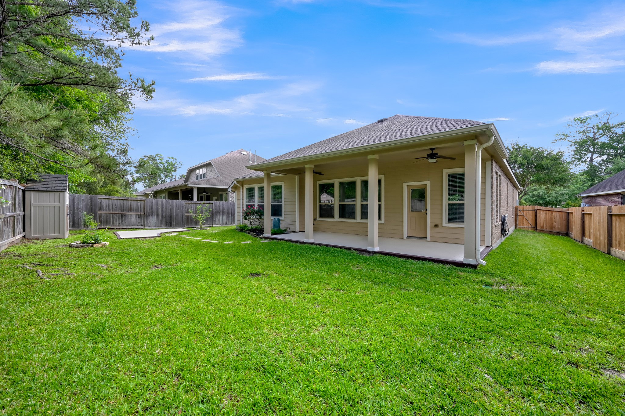 31507 Boulder Cliff Lane Spring, TX 77386 - Photo 38 of 45 This photo showcases a spacious backyard with a well-maintained lawn and a covered patio area. The patio features ceiling fans, providing a comfortable outdoor space for relaxation or entertaining. The yard is fenced, offering privacy and security.