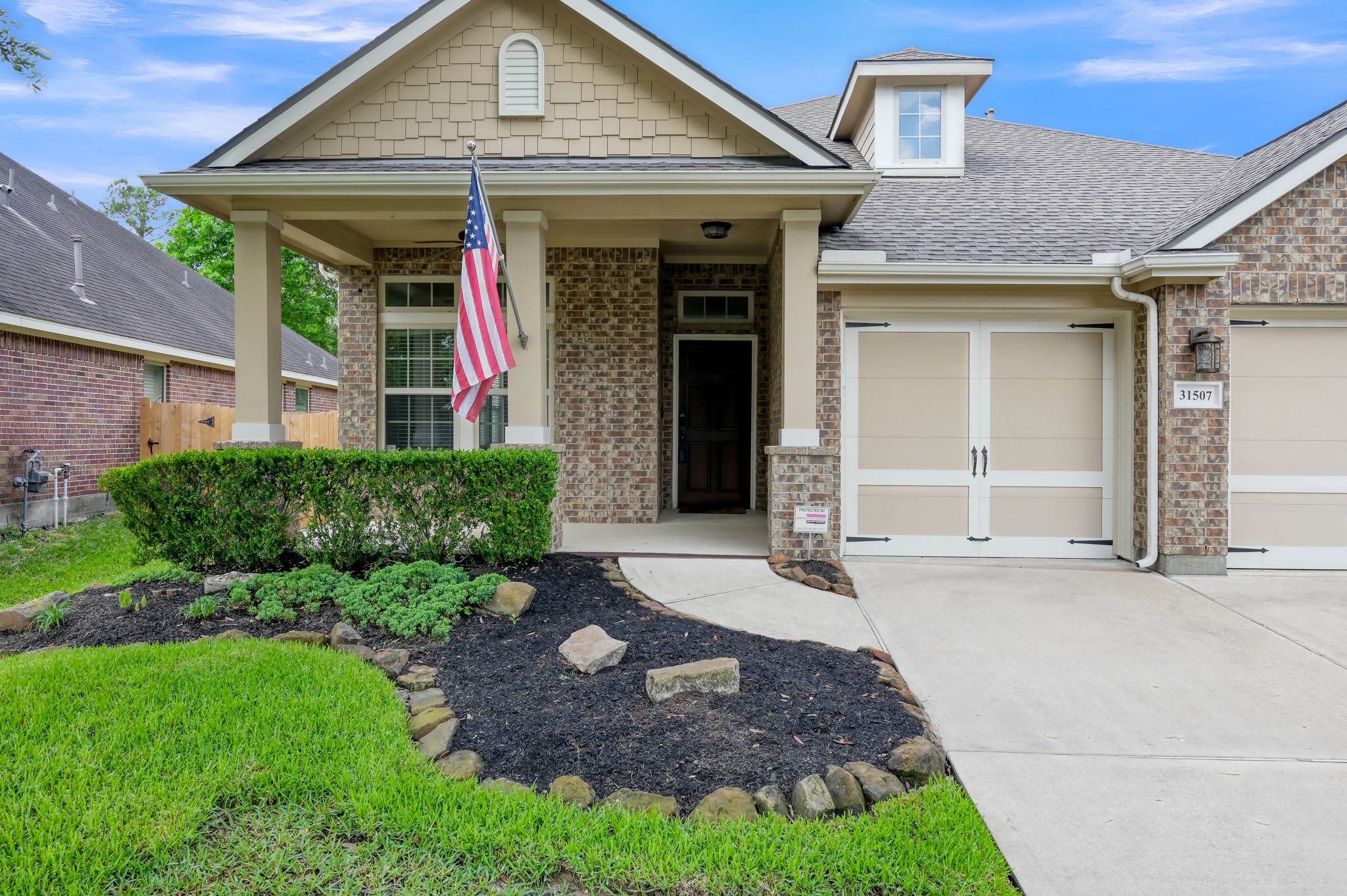 31507 Boulder Cliff Lane Spring, TX 77386 - Photo 44 of 45 Charming single-story home with a welcoming front porch, attractive brick exterior, and well-maintained landscaping. Features a two-car garage with stylish doors and a flagpole by the entrance.