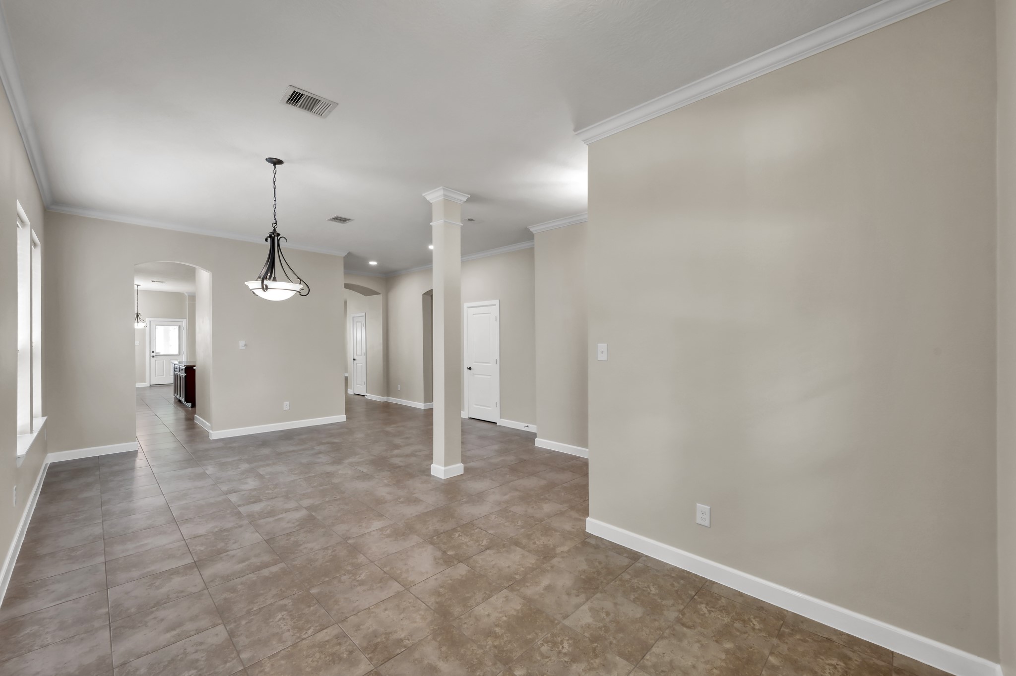 31507 Boulder Cliff Lane Spring, TX 77386 - Photo 6 of 45 This photo showcases a spacious, open-concept living area with neutral-toned walls and tiled flooring. It features a modern light fixture, multiple archways, and natural light from several windows, creating an inviting atmosphere ideal for entertaining.