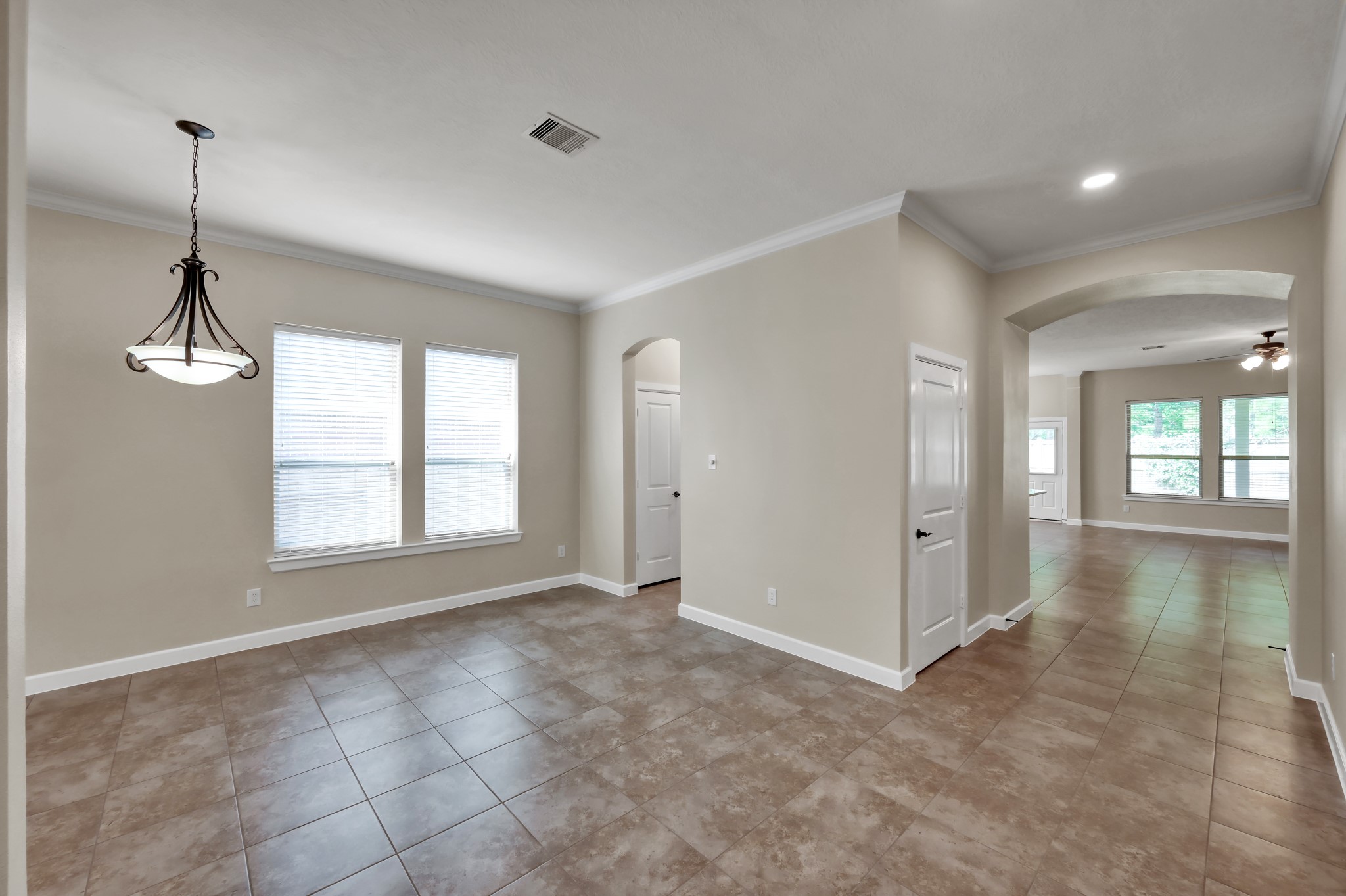 31507 Boulder Cliff Lane Spring, TX 77386 - Photo 7 of 45 This photo showcases a bright, open-concept living area with neutral tones, tile flooring, and abundant natural light from large windows. The space includes a dining area with a hanging light fixture and an arched entryway leading to a spacious room, perfect for family gatherings.