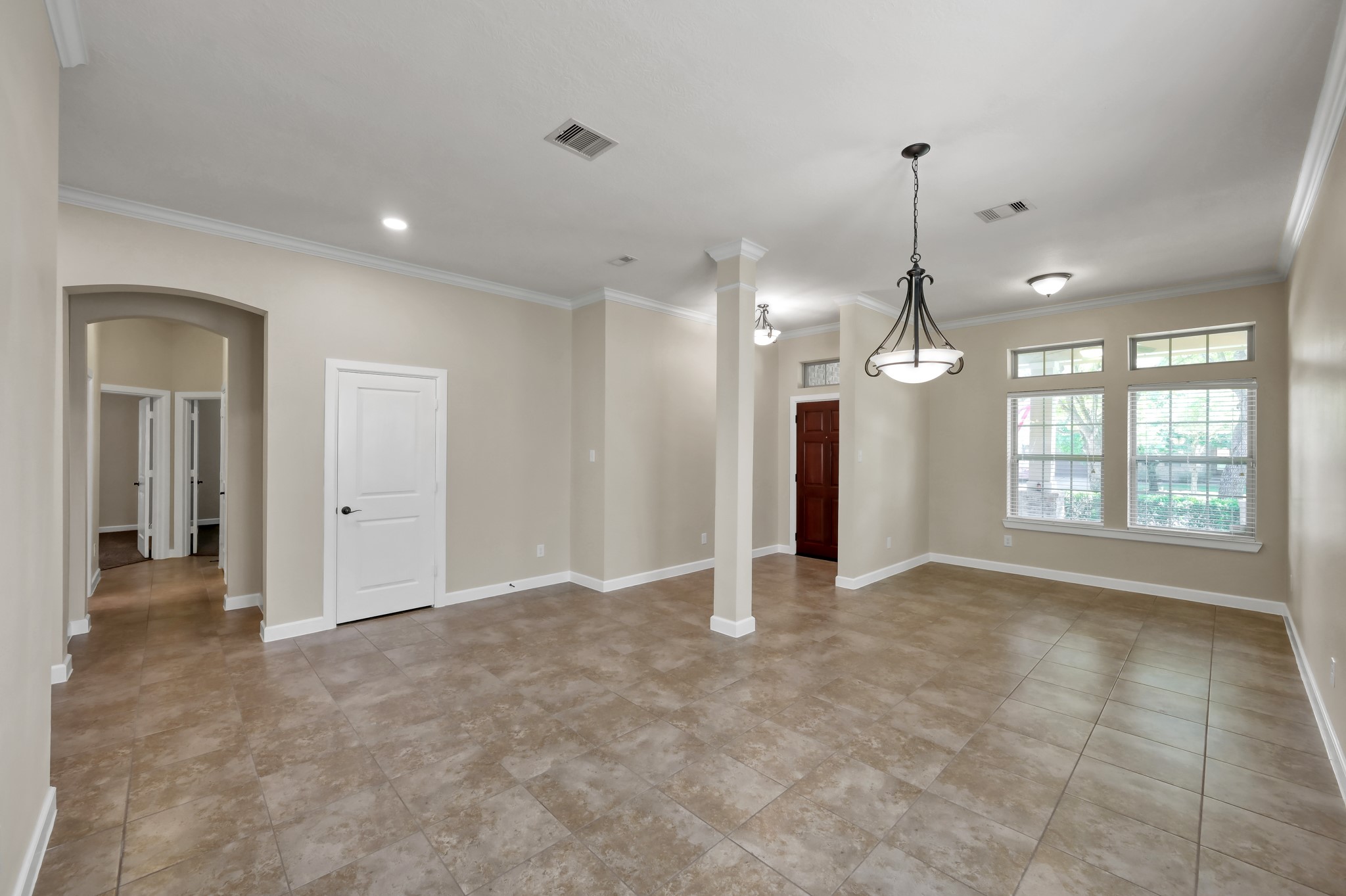 31507 Boulder Cliff Lane Spring, TX 77386 - Photo 9 of 45 Spacious open-concept room with neutral tones, tiled flooring, and ample natural light from large windows. Features modern light fixtures and a versatile layout with access to adjacent rooms and a doorway.