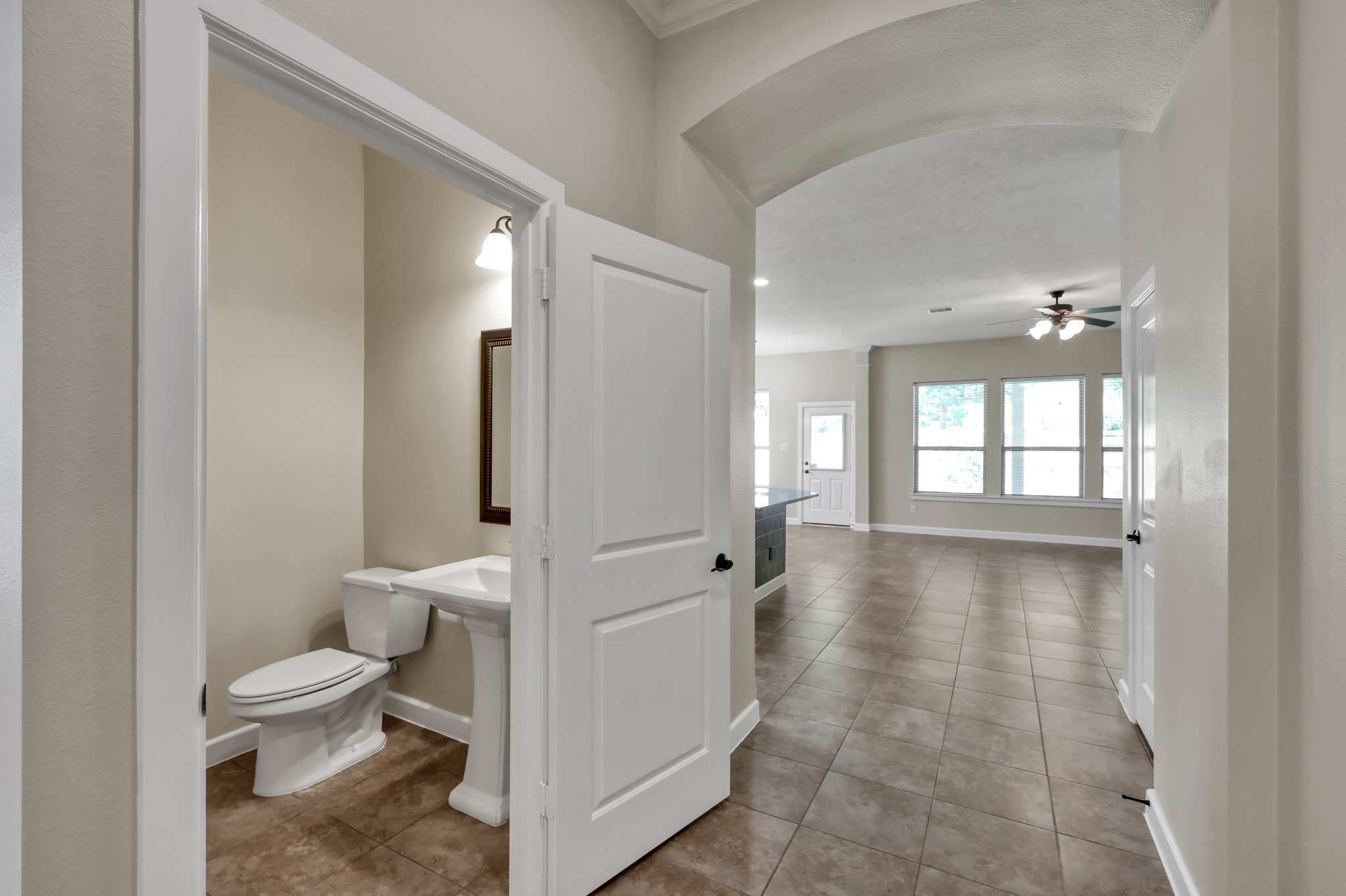31507 Boulder Cliff Lane Spring, TX 77386 - Photo 10 of 45 This photo showcases an open, tiled hallway leading to a spacious living area with large windows. A doorway on the left reveals a convenient powder room with a pedestal sink. The space feels bright and welcoming.