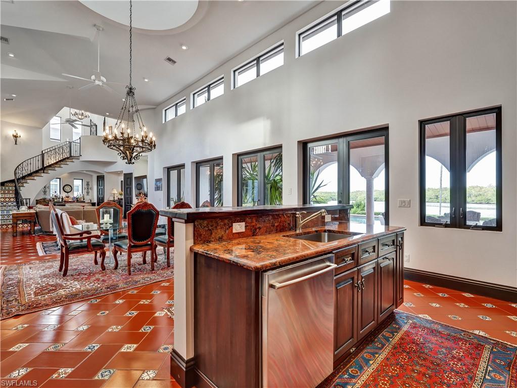 2535 Tarpon Road Naples, FL 34102 - Photo 16 of 50 Kitchen featuring terracotta tile flooring with decorative accents, custom wood cabinetry, a built-in refrigerator, a breakfast bar with a decorative newel post, and high ceilings