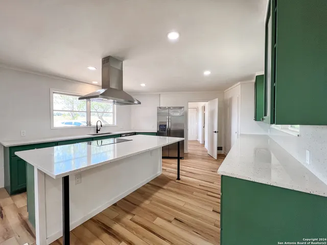 a large white kitchen with kitchen island a sink dishwasher a stove and a refrigerator with wooden floor