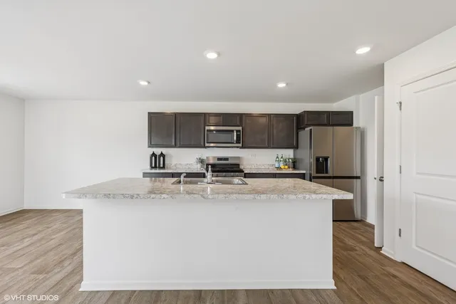 a large kitchen with stainless steel appliances granite countertop a stove a sink a refrigerator and white cabinets with wooden floor