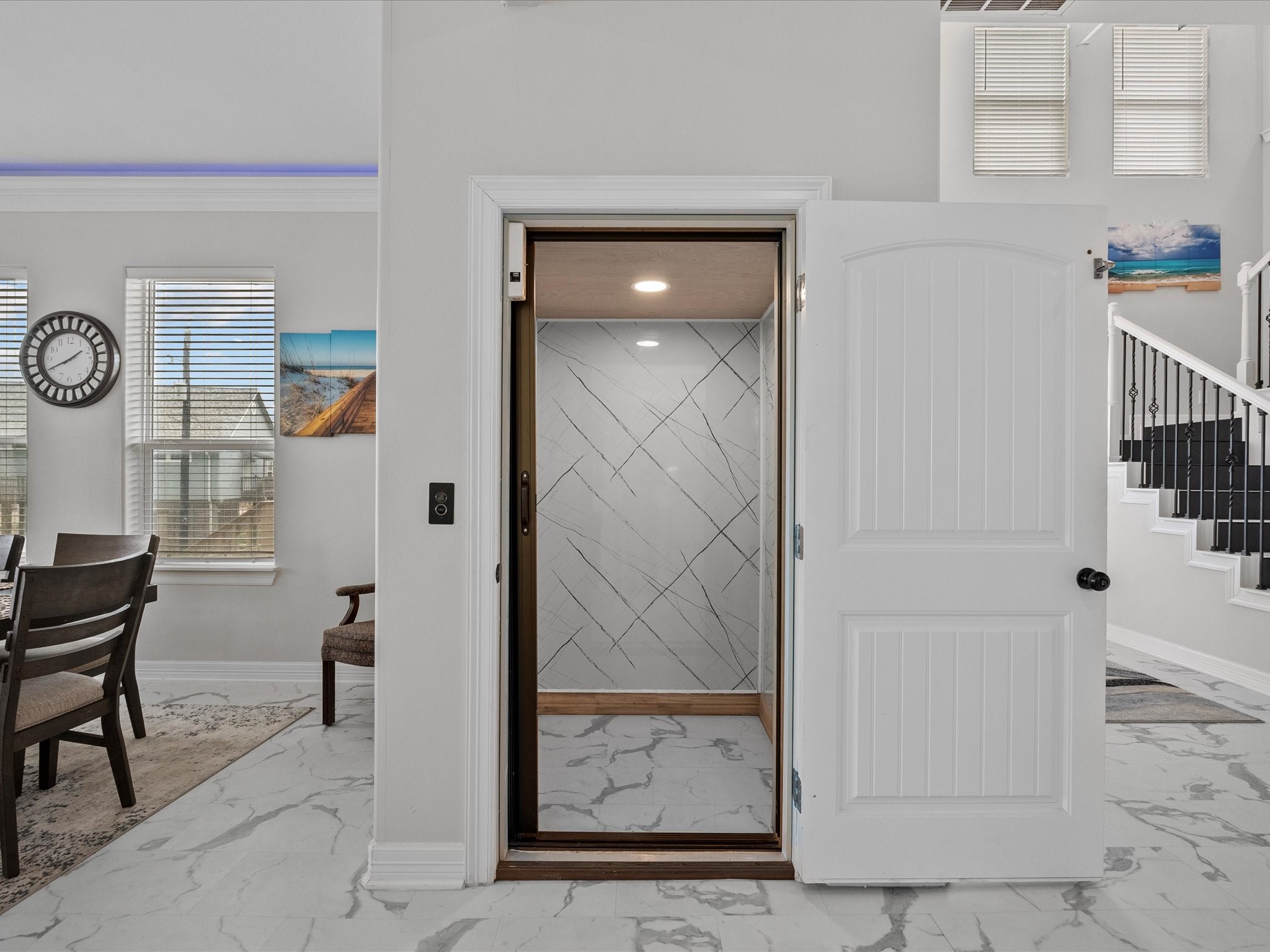 1018 Seashell Drive Surfside Beach, TX 77541 - Photo 24 of 49 This photo showcases a modern home interior featuring a small elevator with elegant marble flooring and walls. The space is well-lit with natural light from large windows in the adjoining dining area. A staircase with black railings adds a stylish touch, enhancing the home's contemporary design.