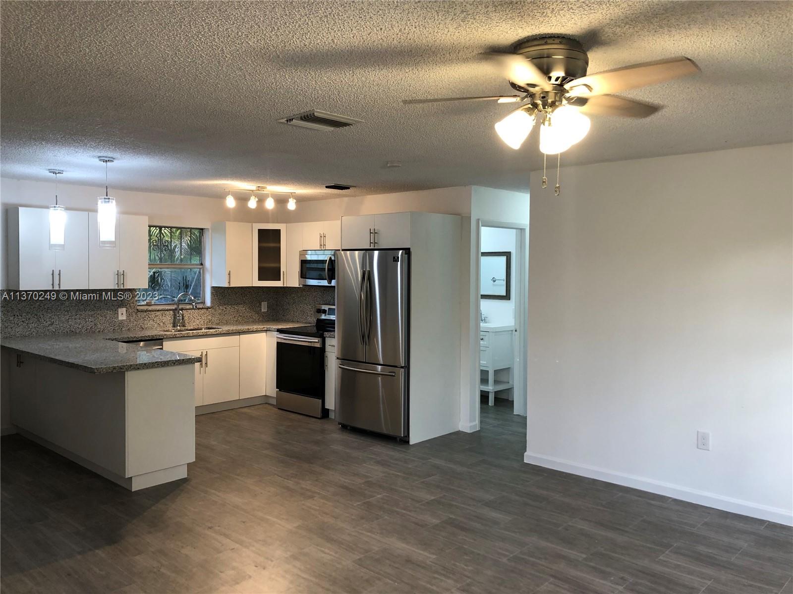 a kitchen with stainless steel appliances kitchen island granite countertop a refrigerator a sink dishwasher a stove and a dining table with wooden floor