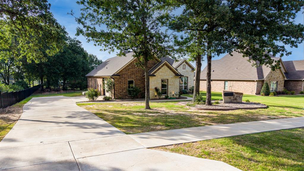 101 Lighthouse Lane Mabank, TX 75143 - Photo 3 of 40 Brick and stone facade residence featuring a concrete driveway, manicured lawn, mature trees, and a decorative stone landscape feature