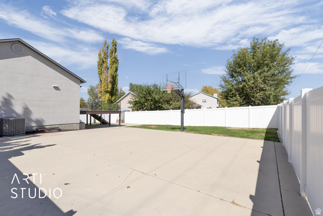 704 West Vahe Street Draper, UT 84020 - Photo 34 of 35 Expansive concrete patio area featuring a basketball hoop, white privacy fencing, and a raised wooden deck with stairs