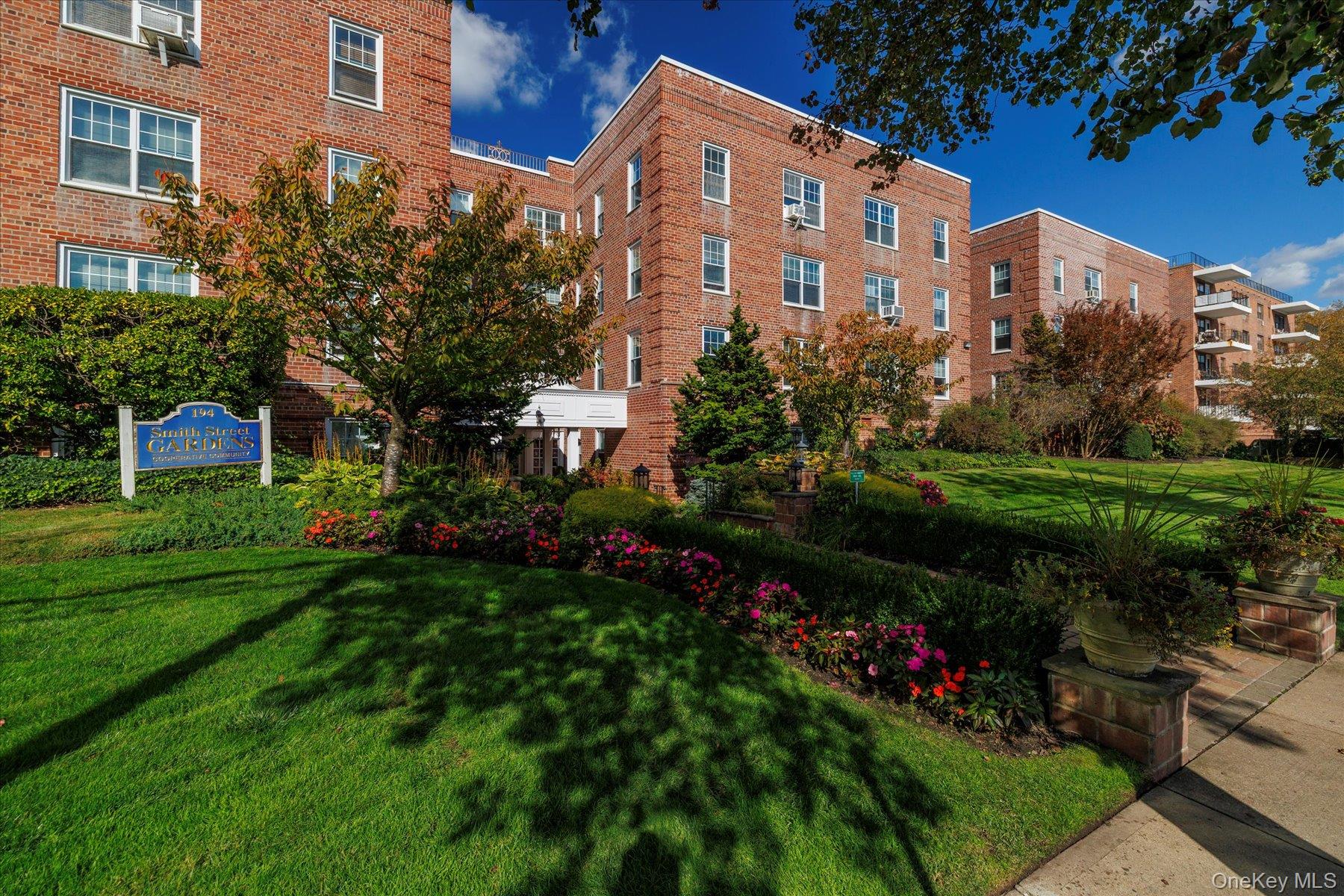 194 Smith Street, Unit 1K Freeport, NY 11520 - Photo 2 of 18 a front view of a house with a garden and trees