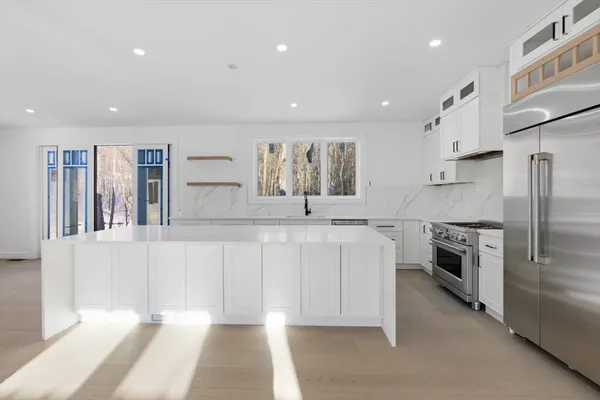 a large white kitchen with stainless steel appliances granite countertop a stove a sink a refrigerator and white cabinets with wooden floor