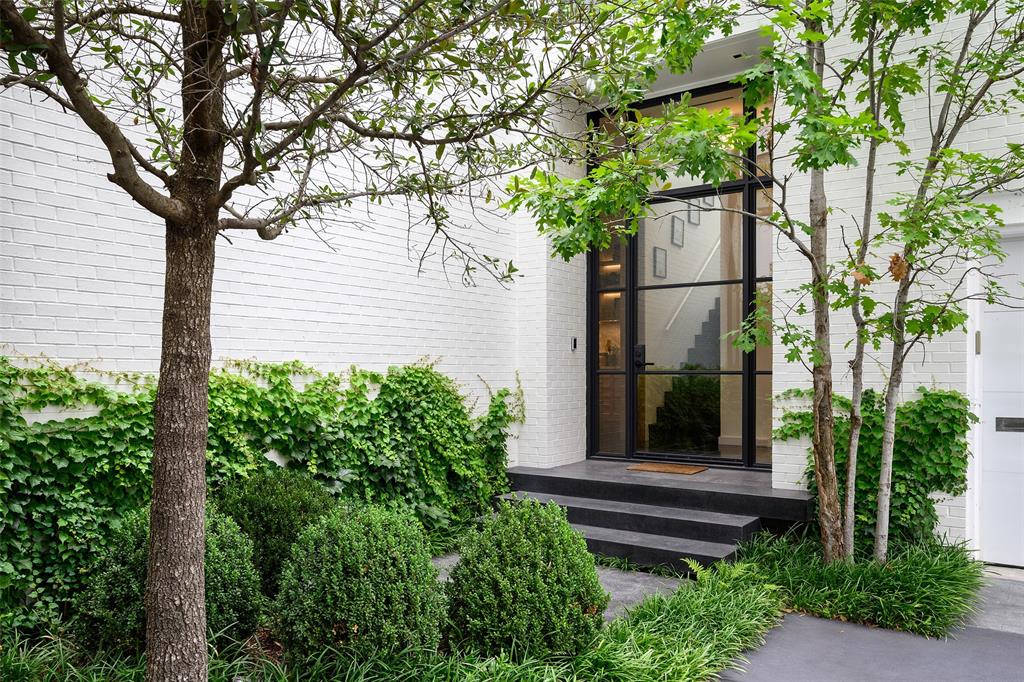 3511 Springbrook Street Dallas, TX 75205 - Photo 38 of 38 Entryway featuring a large glass and black metal framed door, white brick exterior, dark-toned steps, and lush green landscaping