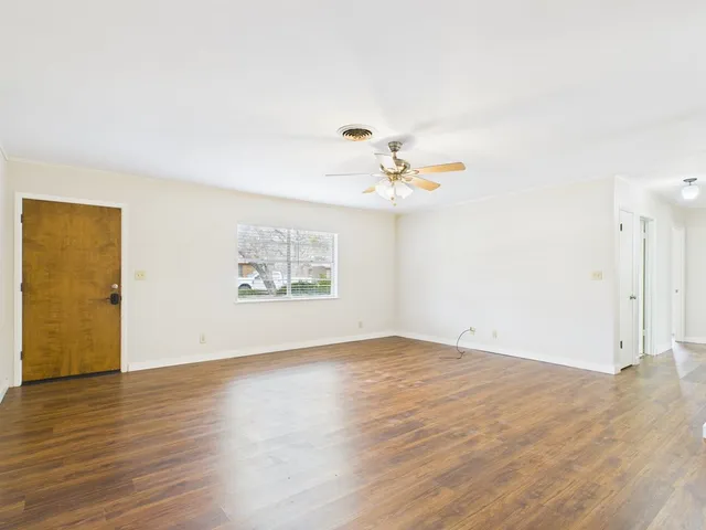 an empty room with wooden floor chandelier fan and windows