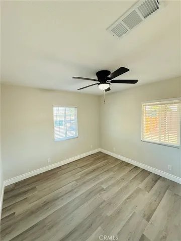 an empty room with wooden floor ceiling fan and windows