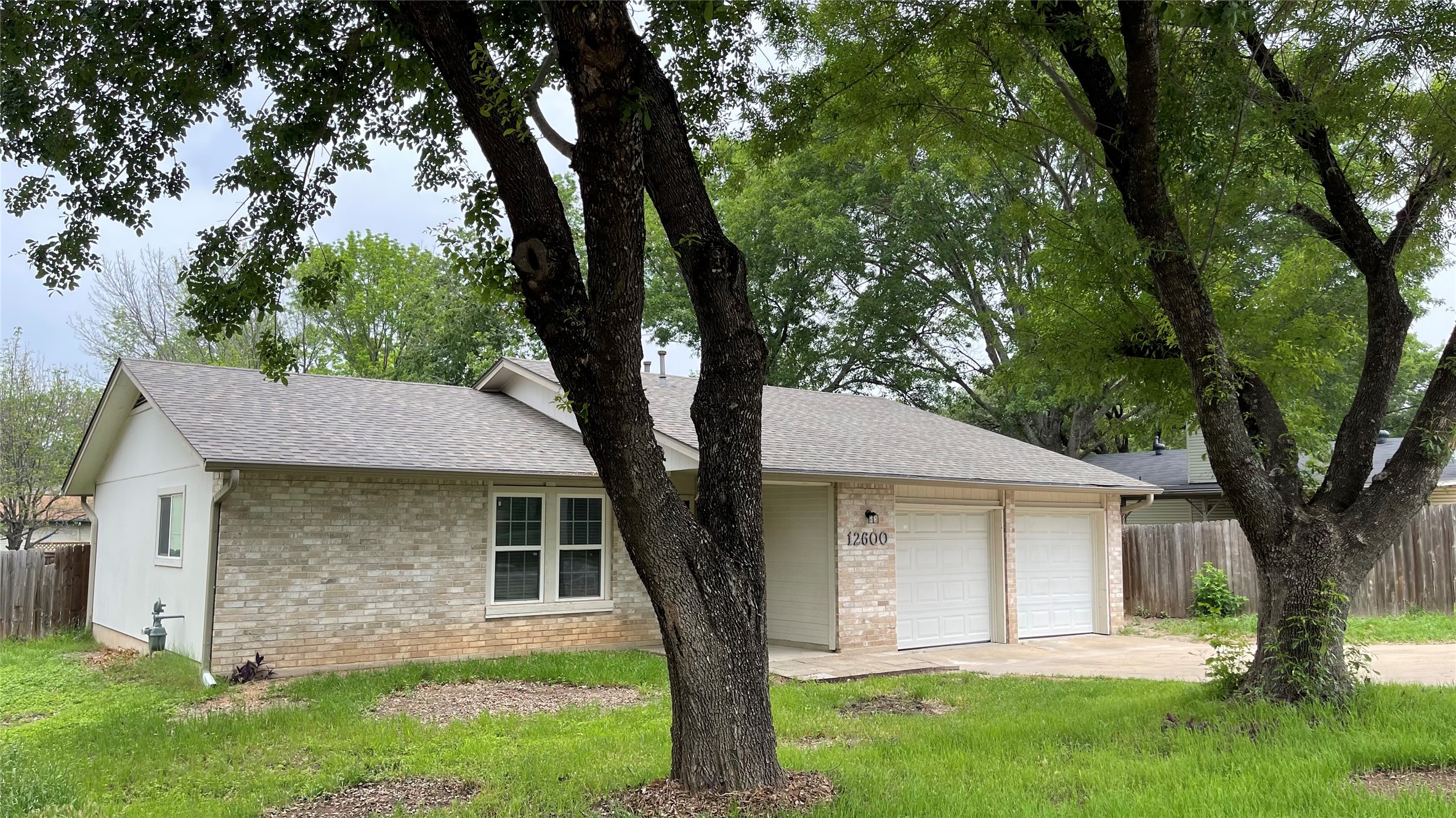 12600 Rampart Street Austin, TX 78727 - Photo 4 of 28 Exterior featuring light brick facade, dual white garage doors, and a gray shingled roof