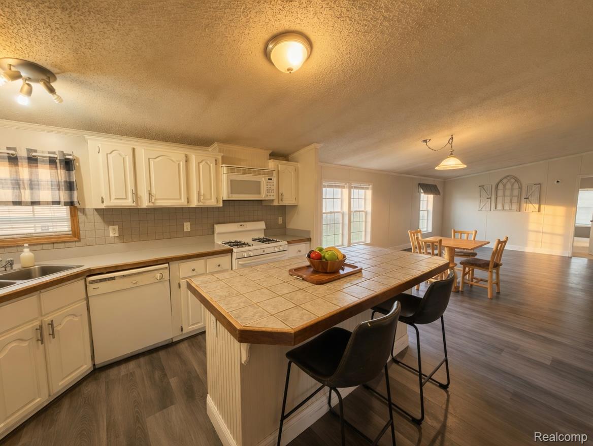 6988 McKean Road Ypsilanti, MI 48197 - Photo 6 of 31 Kitchen featuring dark wood finished floors, white appliances, white cabinetry, a breakfast bar, and a center island