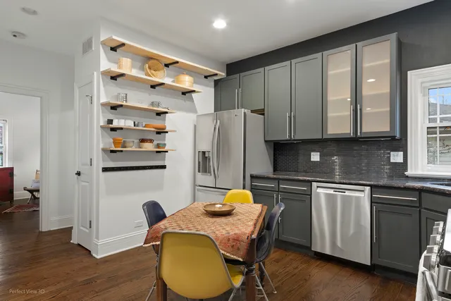 a kitchen with stainless steel appliances granite countertop a refrigerator a sink dishwasher a stove a dining table and chairs with wooden floor